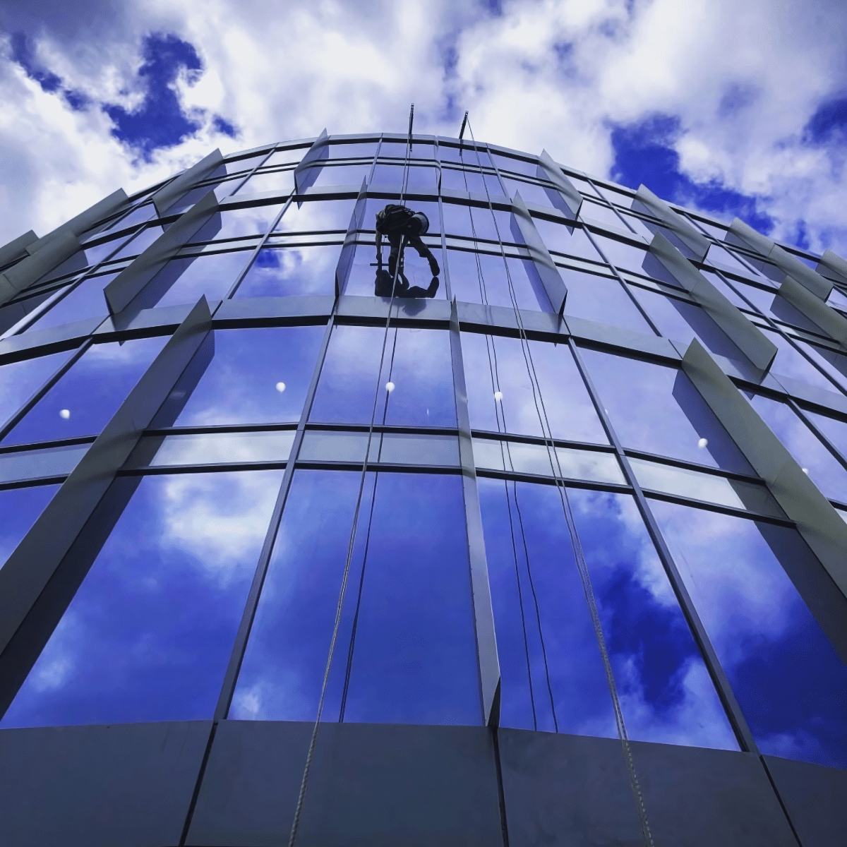 Man on high rise building window cleaning using rope access equipment.