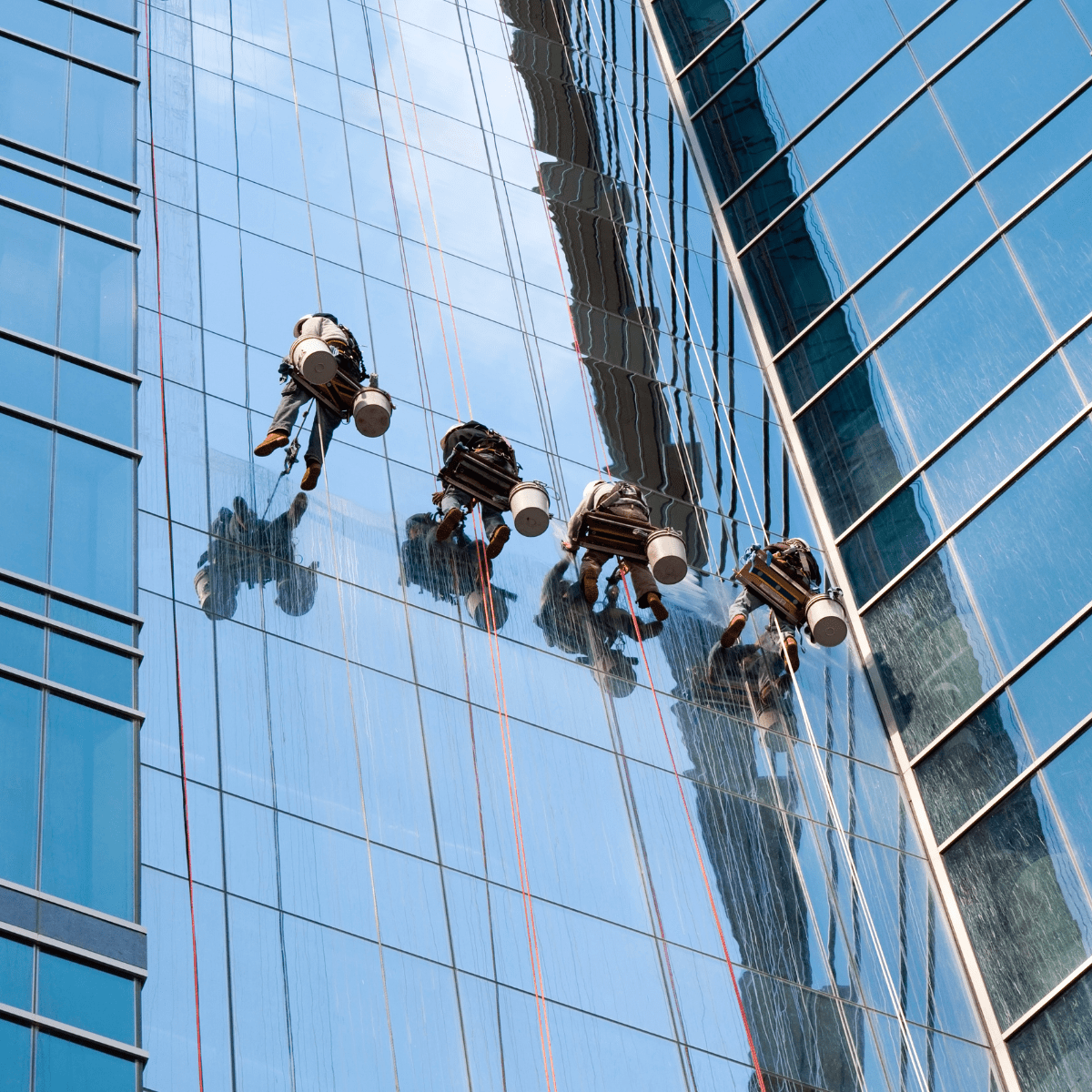 Four men rope access commercial window cleaning high-rise building.