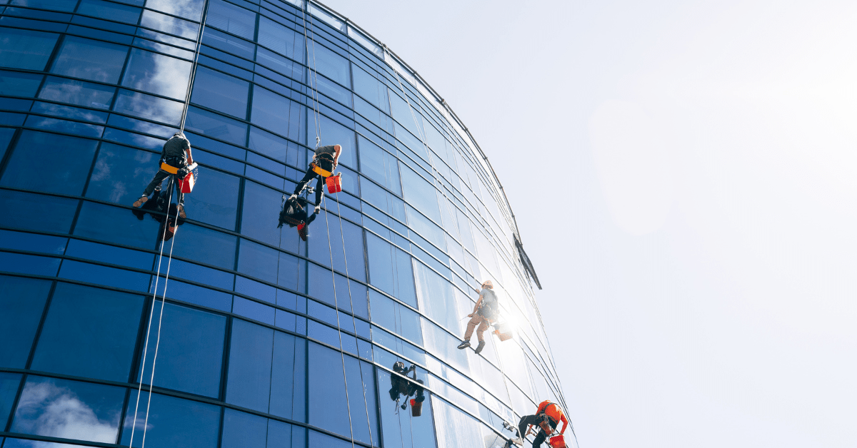 Four commercial window cleaners cleaning glass building facade, using rope access.